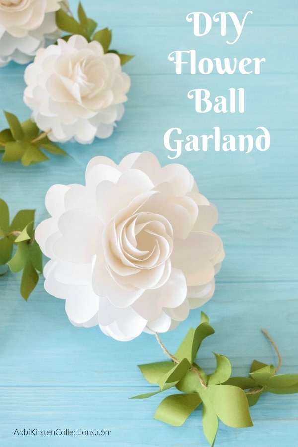 White paper flower balls attached to twine and green leaves, making a DIY flower ball garland.