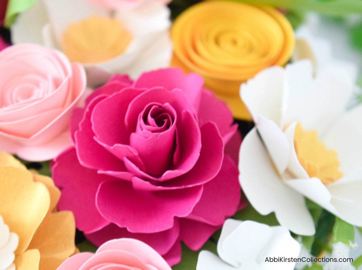 A close up look at the variety of paper flowers in the tea saucer - bright and light pink roses, marigold roses, and white flowers filled with bits of greenery in between.