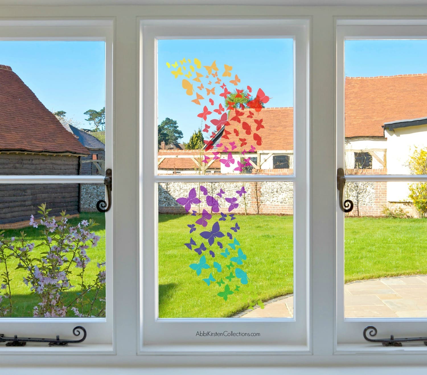 Three large double pane windows look out into a bright and sunny backyard with green grass. On the center window is a wave of rainbow butterflies in various sizes.