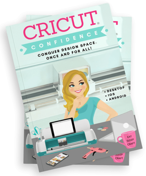 An overhead view of Abbi Kirsten's book called "Cricut Confidence - conquer Design Space once and for all!" The book cover is an illustrated picture of Abbi in her craft room with her Cricut machine. 