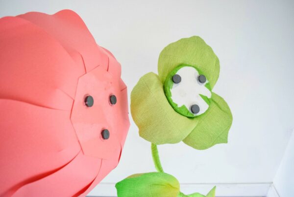 The giant red paper flower has three magnets, and are being placed on the three magnets on the top of the free-standing green stem. 