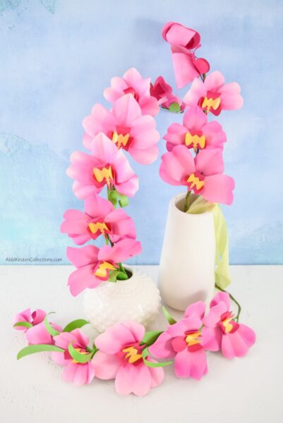 Two vases filled with stands of pink and yellow paper orchids that look so real and are easy to make using this tutorial. 