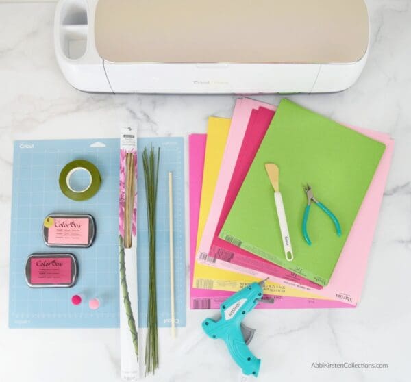 Laid out on a white marble tabletop are the supplies needed to make easy DIY paper orchid flowers. Note you do not need a Cricut cutting machine, but it certainly helps!