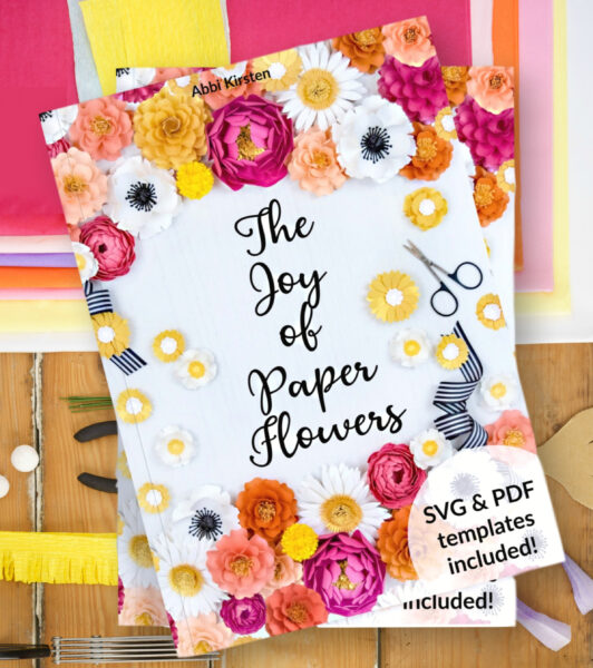 The book cover for Abbi's eBook titled "The Joy of Paper Flowers". The book cover has a white background filled with colorful paper flowers and crafting supplies.