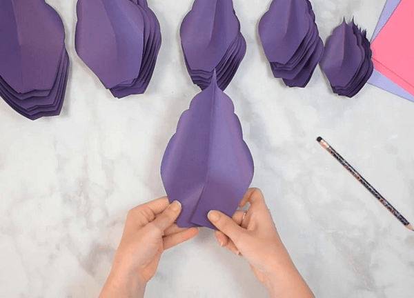 Stacks of prepared purple amaryllis paper flower petals are ready to use. Abbi demonstrates how to overlap the petal slit ends to create the petal’s shape. 