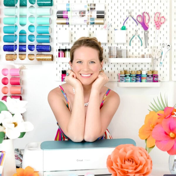 Abbi Kirsten Collections. Abbi smiles in her craft room, surrounded by paper flowers and supplies organized on the wall. 