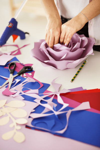 Amid scraps of blue, violet, and red paper, as well as supplies like scissors and a glue gun, Abbi glues in the final petals in her giant paper flower craft.