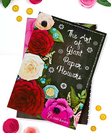 The cover of Abbi Kirsten's book titled "The Art of Giant Paper Flowers". The book cover has a dark background filled with red, white, and pink paper flowers.