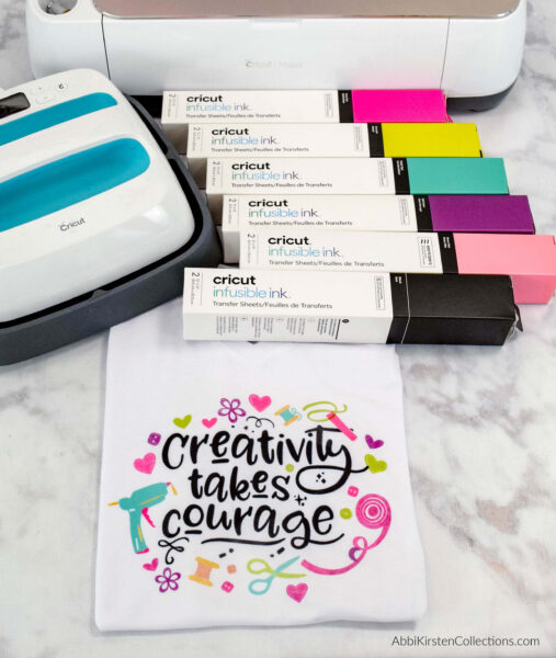 Creativity takes courage, so don’t be afraid to try all the colors Cricut Infusible Ink has available. A photo of A Cricut machine, easy press, boxes of infusible ink, and a folded t-shirt with "creativity takes courage" written in black and surrounded by colorful craft supply illustrations. 