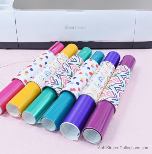 Did you know you can upcycle cardboard tubes to organize your craft vinyl? These upcycled cardboard tubes decorated in bright rainbow-print paper hold pink, yellow, green, blue, and purple colored craft vinyl.