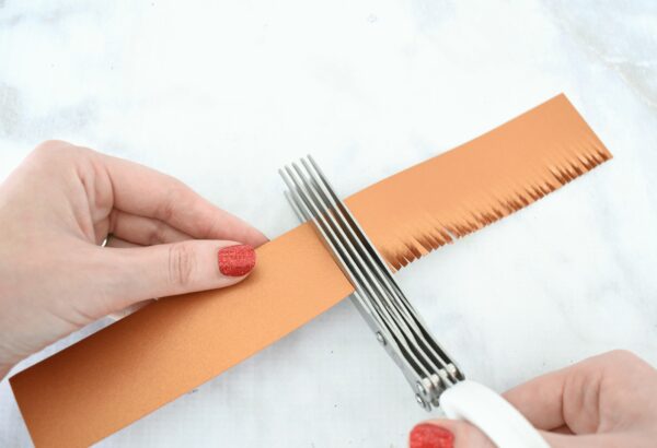 Abbi demonstrates how to use fringe scissors to cut a brown strip of cardstock to make the sunflower center. 