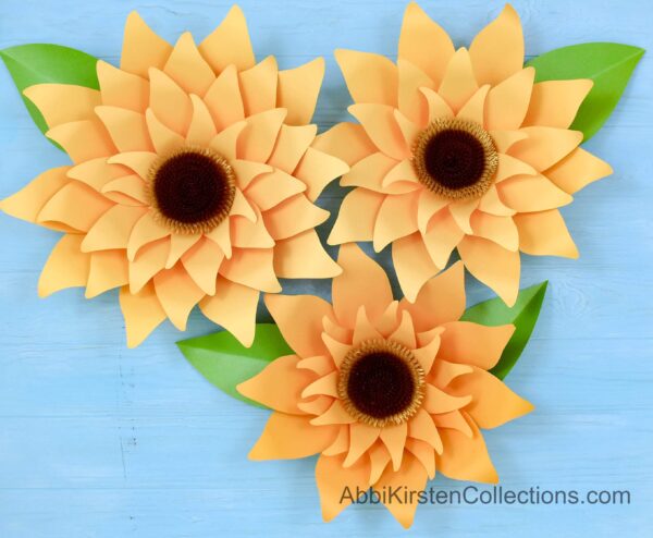 Three yellow, giant paper sunflowers decorate a light blue table. Paper sunflowers make great background art for any room. 