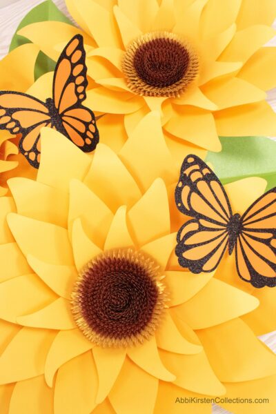 A closeup of brown centers of two giant large paper sunflowers with butterflies. You can learn how to make these giant flowers. 