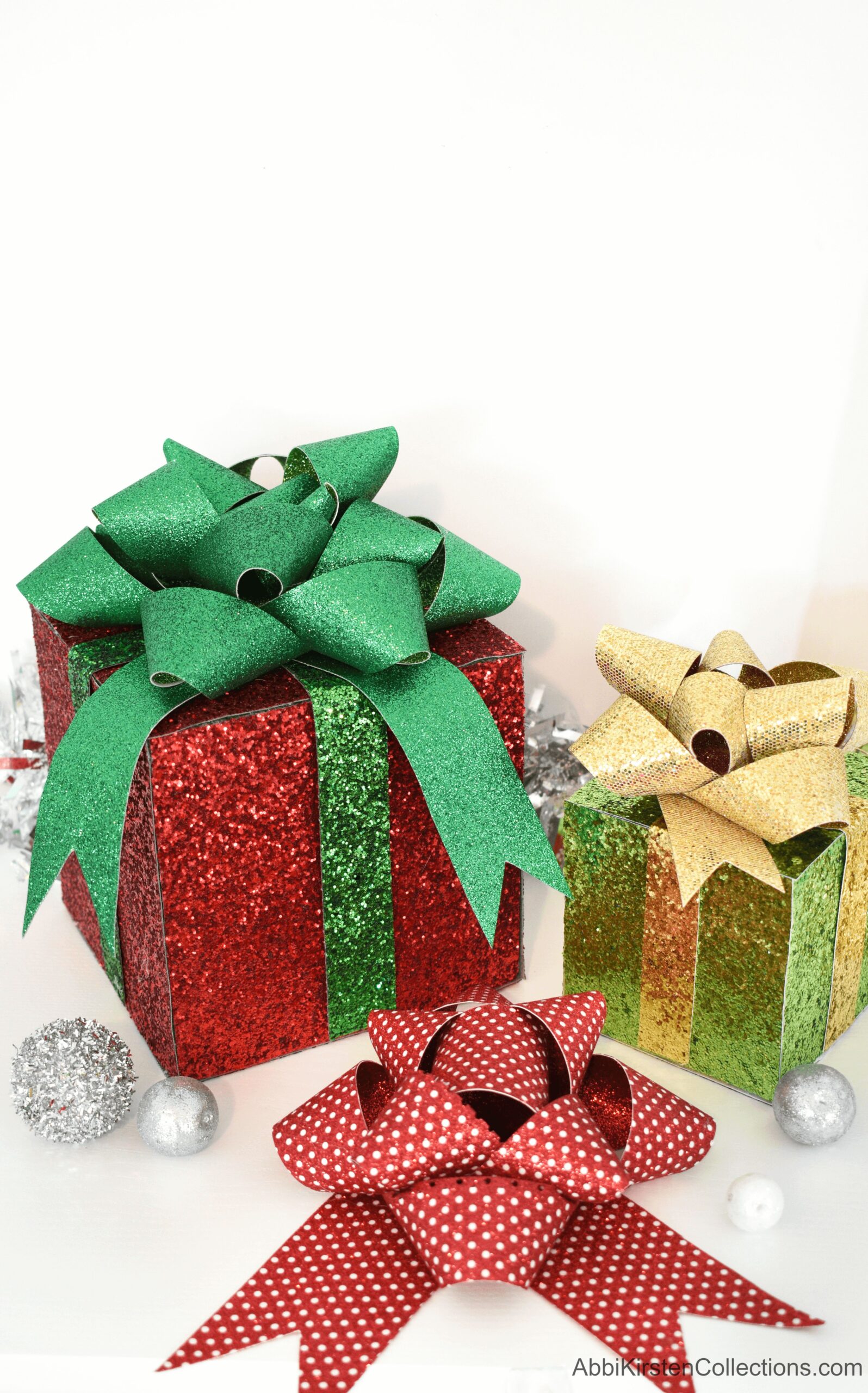 Two decorative gift boxes made with faux glitter leather sheets. One box is red with a green bow, and a smaller box is light green with a gold bow. A red and white polka dot bow sits between the gift boxes.
