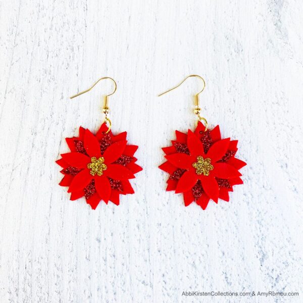 Red Poinsettia faux leather earrings with gold earring hooks on a white workspace. 

