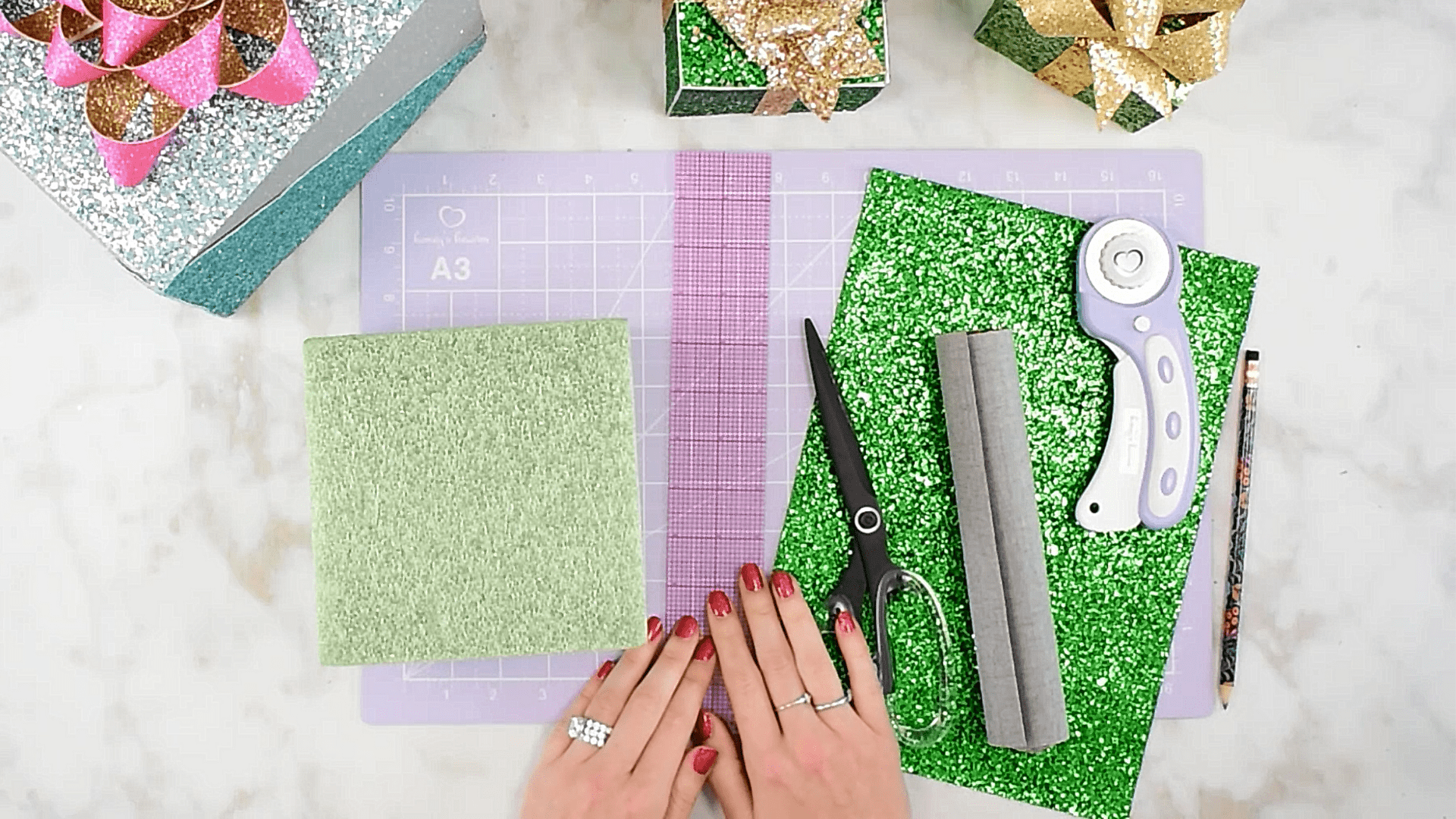 Crafting supplies laid out on a marble table includes a cutting mat, sheets of faux glittery leather, and crafting tools.