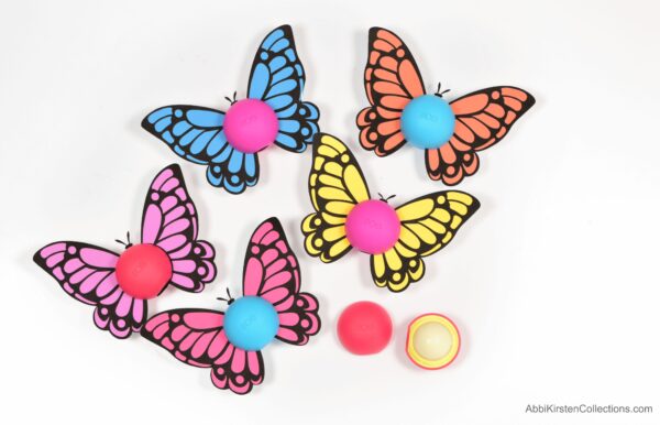 Five varing colors of free butterfly printables surrounding Eos lip balms lay on a white table next to an open Eos lip balm. 