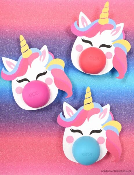 Three happy, colorful unicorn heads have Eos lip balm as noses. These templates are available for free and make great gifts. 