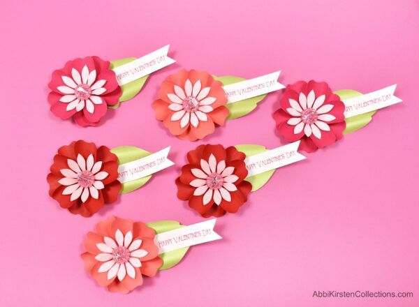 Six pretty red and pink paper flower Kiss candy valentines arranged on a hot pink table. 