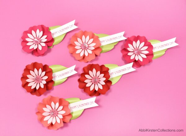 Six pretty red and pink paper flower Kiss candy valentines arranged on a hot pink table.