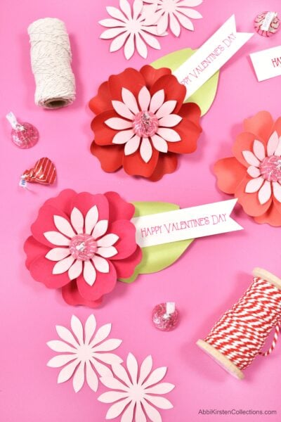 Red and pink DIY Paper Flowers for Kiss Candy Valentines on top of a hot pink workstation. 