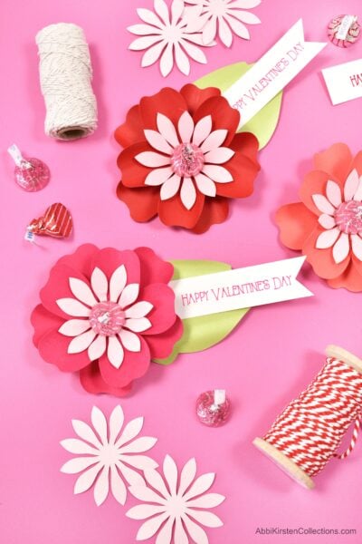 Red and pink DIY Paper Flowers for Kiss Candy Valentines on top of a hot pink workstation.