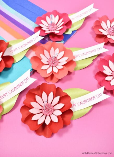 Several red and pink Paper Flower Kiss Candy Valentines alongside multicolored craft paper.