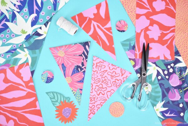 Colorful wrapping paper cut into triangles, circles and flowers alongside black scissors and white twine.