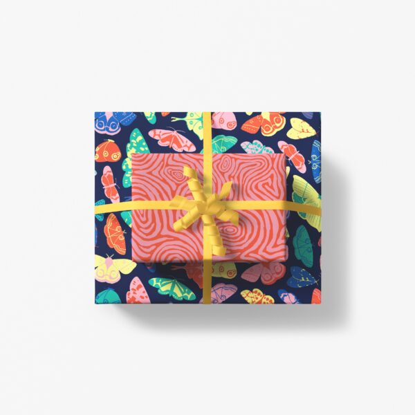 A box wrapped in colorful butterfly wrapping paper topped with a box wrapped in pink and red swirls wrapping paper tied together with a yellow ribbon, all sitting on a white table. 