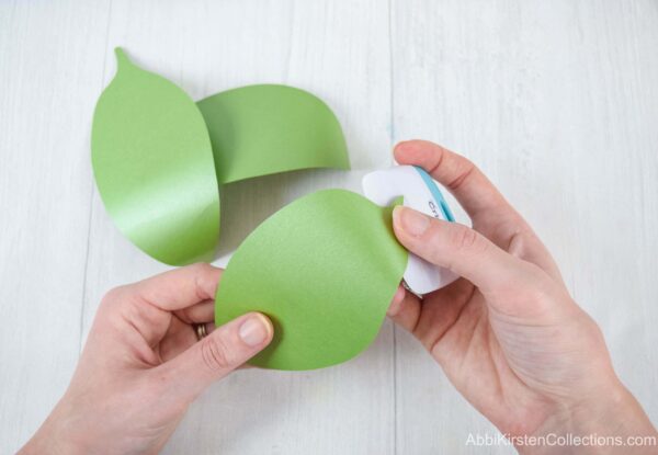 A woman’s hand demonstrates how to curl paper leaves using a scraper edge. These leaves will be at the bottom of the bouquet base to support the paper flowers. 