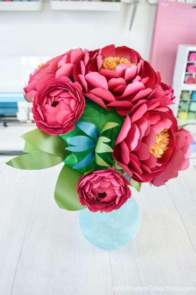 The cascading paper flower bouquet sits in a vase for easier crafting. The tissue paper-covered foam base is visible in some spots but will be hidden by adding more small flowers and greenery. 