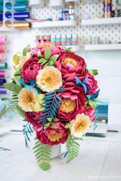 A colorful, completed cascading paper flower bouquet sits finished in a small vase. You can use this lush, beautiful bouquet for special events like weddings or just as decoration. 