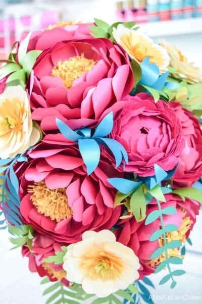 A close-up view of a completed paper flower arrangement. The mix of blue, red, green, yellow and white in the flowers, leaves and vines is lovely for spring or summer events. 