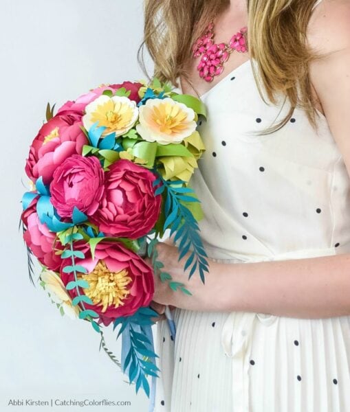 Side view of a woman in a white dress holding a colorful DIY cascading paper flower bouquet that can be used as an alternative to live flower bouquets in weddings and other special events. 