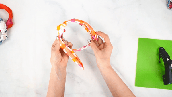 In this overhead view, Abbi glues the ends of the top knot onto the ends of the wrapped headband and glues the ends down securely. 