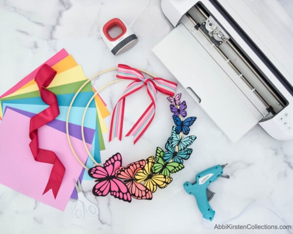 Use your Cricut machine and Easypress mini to create home decor with this colorful butterfly DIY wreath for Spring. Make paper butterflies with cardstock and iron-on vinyl to add to an embroidery hoop!