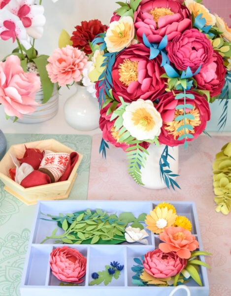A colorful paper flower bouquet in a white vase next to pieces to create a flower arrangement. 