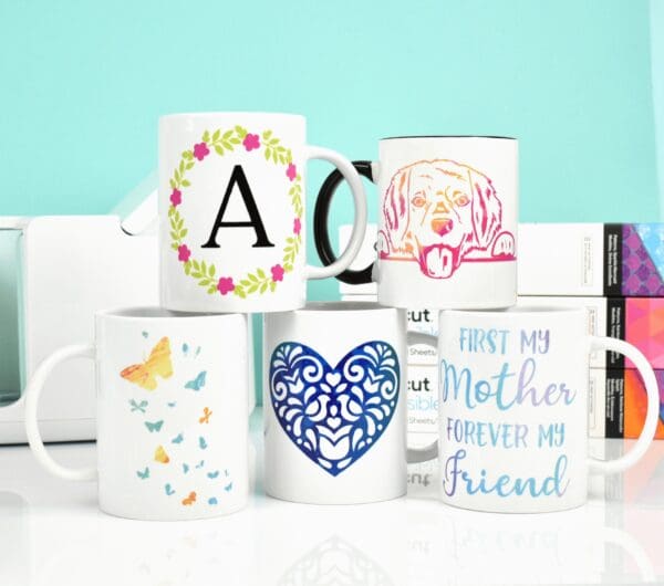 A stack of DIY mugs with a Cricut Joy machine and infusible ink boxes. 