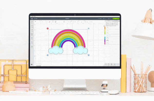 A rainbow with clouds is a design in Design Space, as seen on this monitor on top of a pink-hued desktop. 