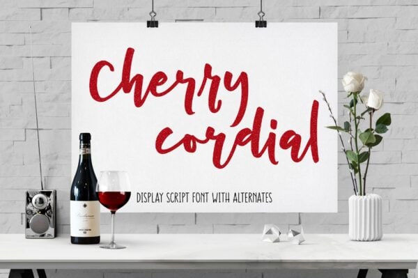 A picture of a white table in front of white brick, with white roses, a transiter radio, and a bottle of red wine with red wine in a glass next to it. A white sign has a handwritten cursive font in red called "Cherry Cordial" listed as a "display script font with alternatives."