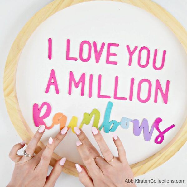 Wooden letters cut with a Cricut machine are placed by Abbi Kristen into a wooden circle. It reads "I love you a million rainbows."