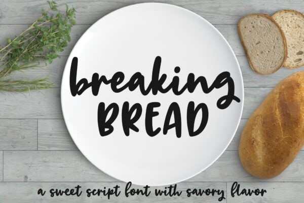Breaking bread is written in black on a white plate. Herbs lay tp the left and bread  lays to the right on a gray wooden table. It is described as a 'sweet script font with a savory flavor.'