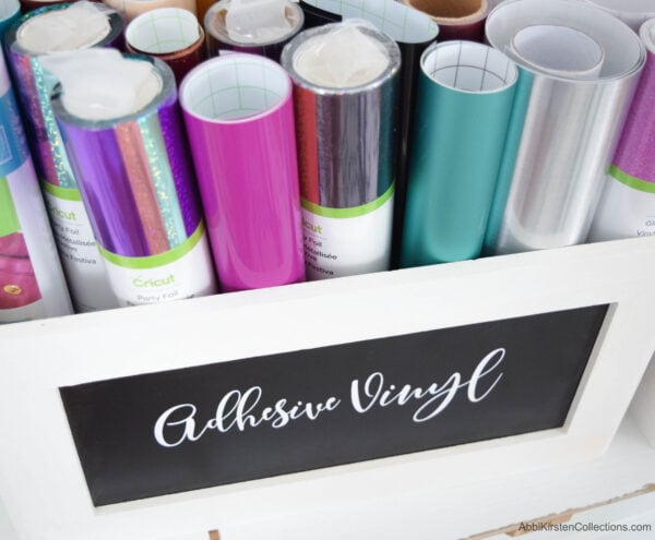 Rolls of multiple-colored adhesive vinyl rolls in ai storage box labelled "adhesive vinyl." 