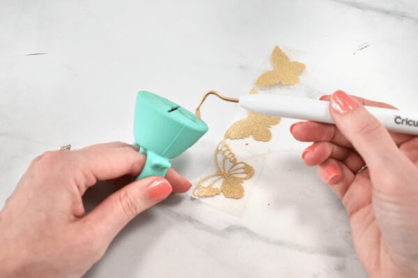 A woman's hands demonstrate how to weed vinyl with a Cricut weeding tool an a scrap catcher worn like a ring on her left hand. These vinyl hacks will make crafting with your Cricut machine much easier. 