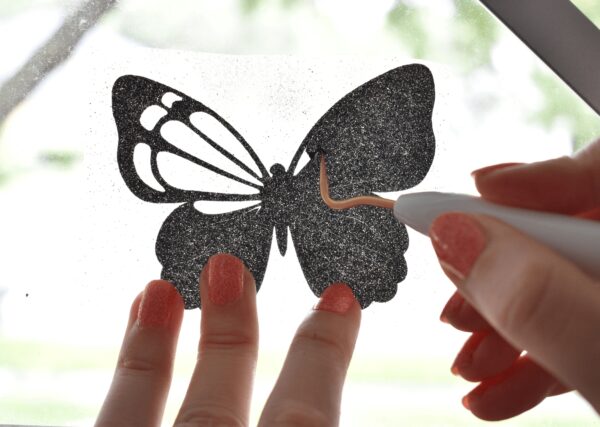 A closeup of a vinyl black butterfly, held up to a window to make weeding the vinyl easier. You can use a window or a Brightpad to make vinyl crafting easier. 