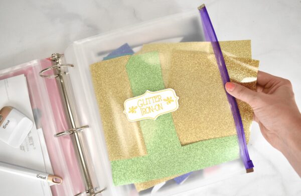 A clear zipper binder pouch is used to store scraps of glitter vinyl. A binder and zippered pouches are great ways to organize your Cricut vinyl. 