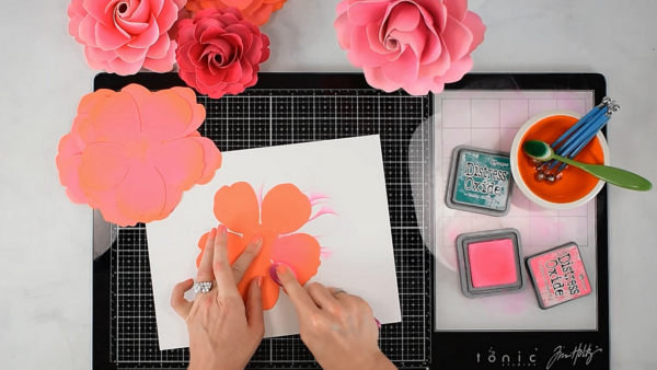 A paper rose petal distressed with pink ink on a black work station.