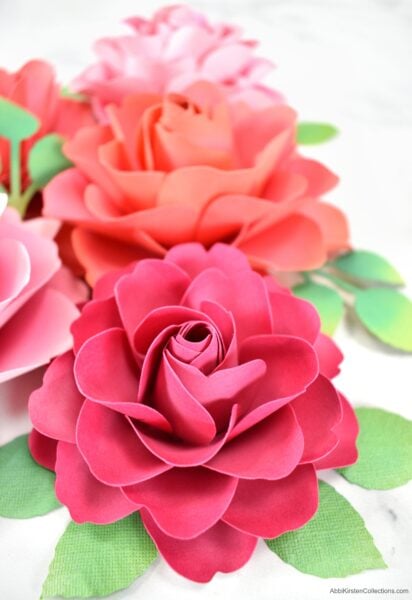 Beautiful red and pink 7-petal paper flowers with light green leaves on a marble counter. 