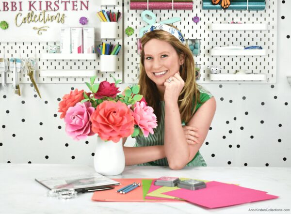 Abbi poses with a handmade rose arrangement in a white vase. This paper rose tutorial can be used by anyone, including beginners, to make full bloom garden roses for decoration, wedding bouquets, and much more. 