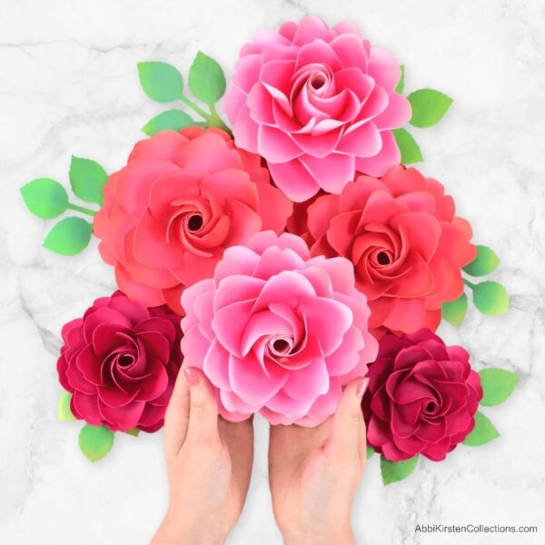 A bouquet of red and pink paper roses with delicate green paper leaves against a marble background.